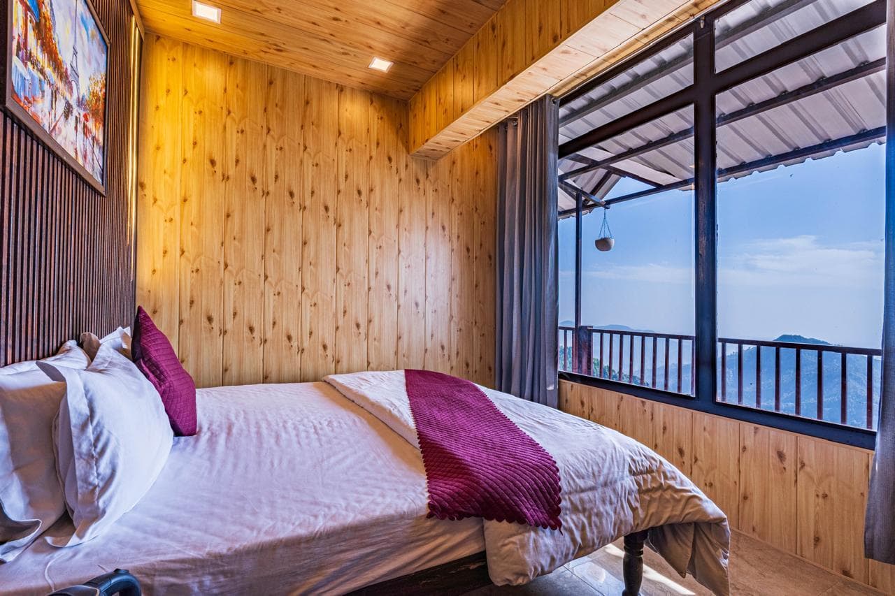 Bedroom at Spandan Villas with timber walls, glass balcony doors, and Dhanaulti valley views